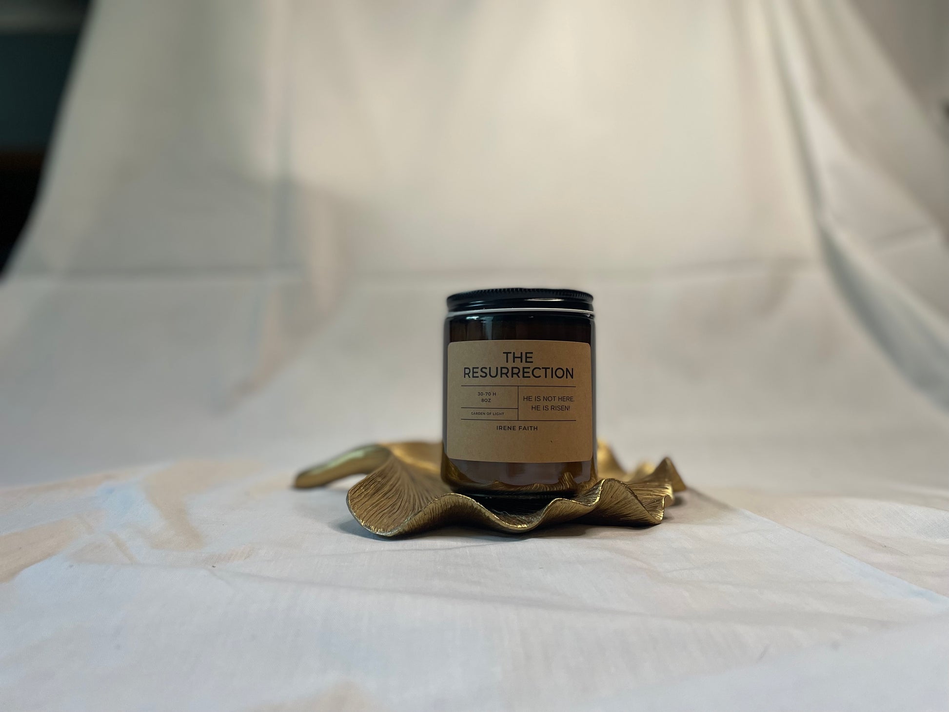 Candle labeled 'The Resurrection' on a decorative brass holder against a white background